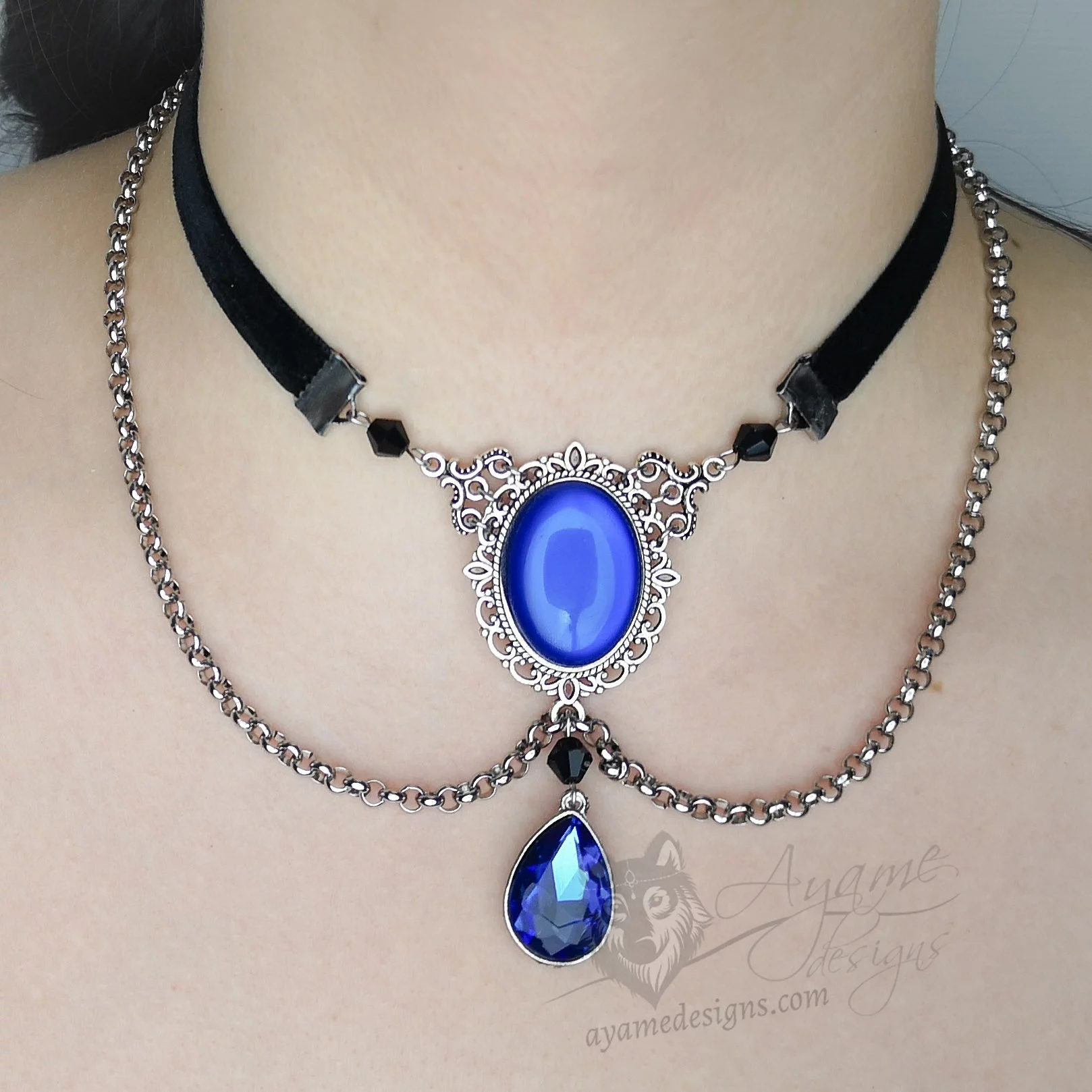 Handmade adjustable black velvet choker necklace with Austrian crystal beads, a large blue resin cabochon pendant in a silver filigree frame, and a blue teardrop pendant, with chain details