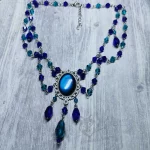 An adjustable gothic beaded choker necklace with blue and teal Austrian crystal beads and a blue resin cabochon inside a silver filigree frame
