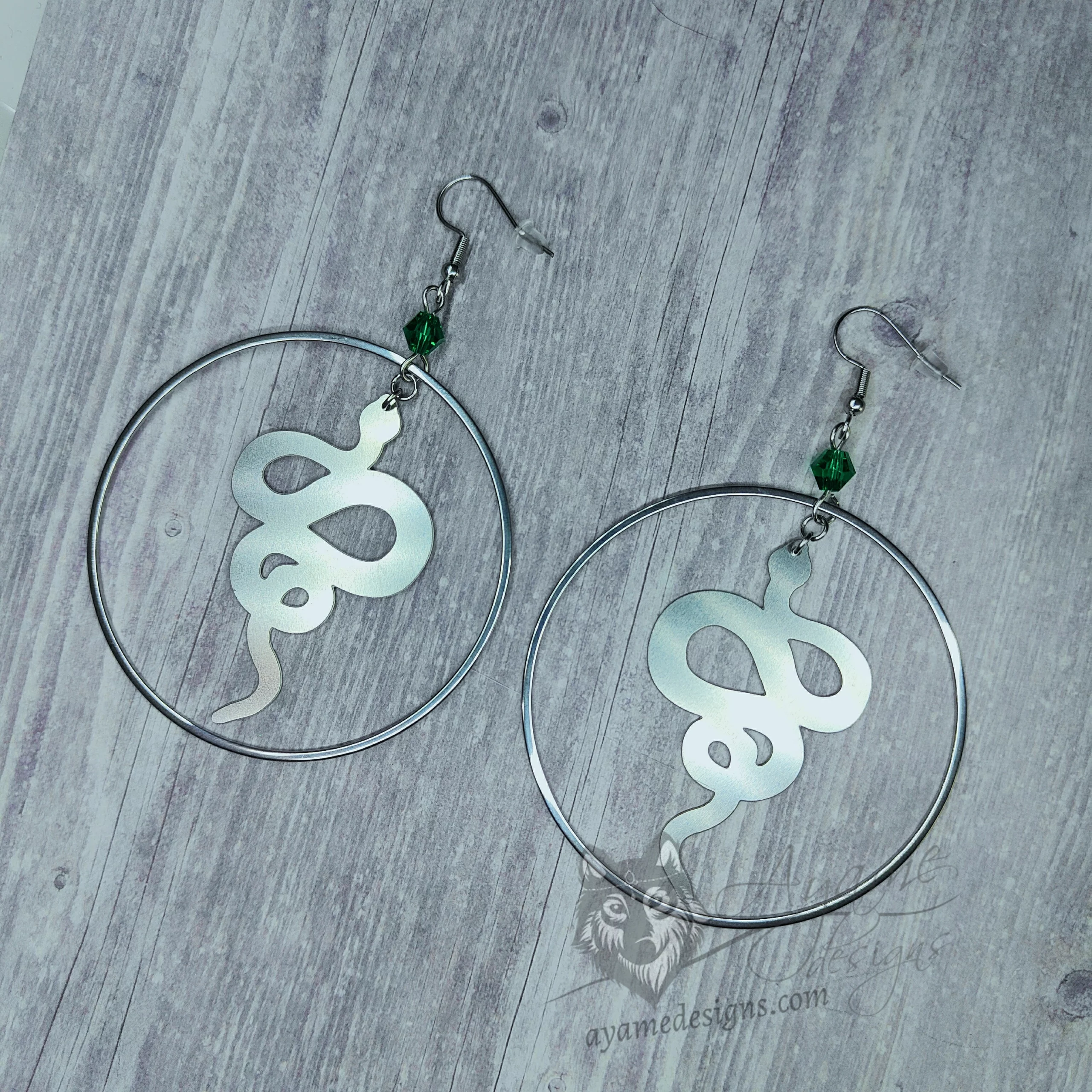 Handmade earrings with laser cut stainless steel snake charms inside large stainless steel rings with green Austrian crystal beads, on stainless steel earring hooks