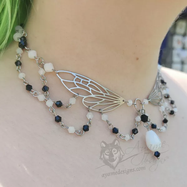 An adjustable cottagecore fairycore fantasy beaded choker necklace with white and black Austrian crystal beads and stainless steel laser cut fairy wings