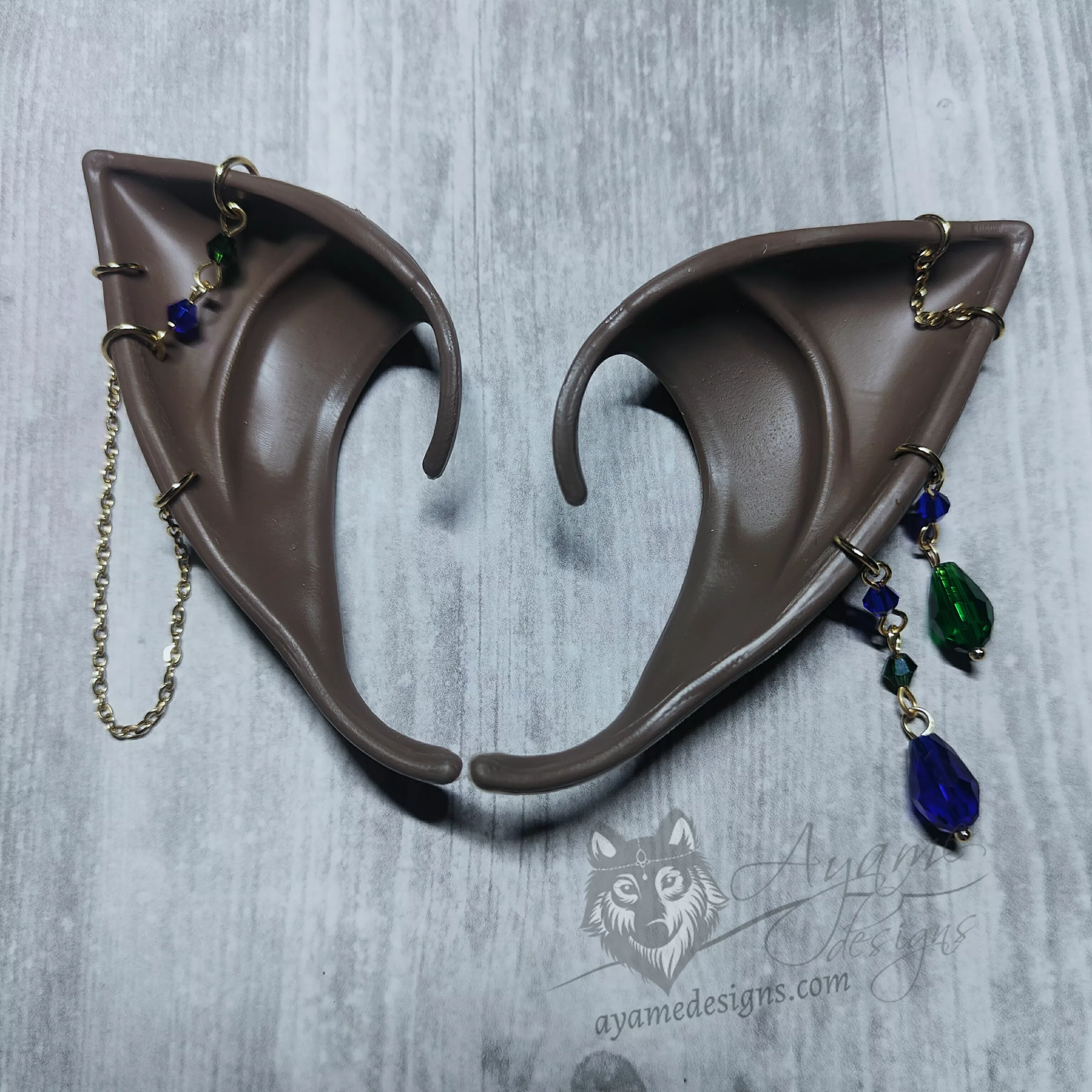 Dark brown skinned elf ears with many gold chains, and blue and green beads