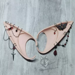 Pink toned beige elf ears with silver chains and rings, red and black glass beads and a dagger and death head moth charms